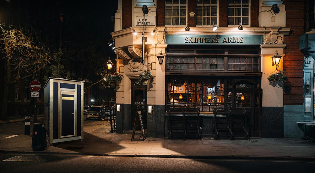 Porterhouse 25 Portable Restroom Near a Corner Bar at Night with Lampost